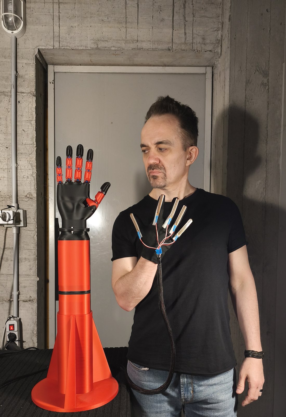 Andrea Milani nel suo laboratorio, con il guanto di sensori di flessione alla mano e la mano teleoperata stampata in 3D accanto a lui.