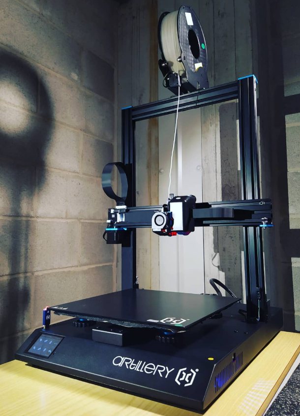 La stampante 3D Artillery SideWinder X1 con la bobina di filamento montata, davanti a un muro di cemento.