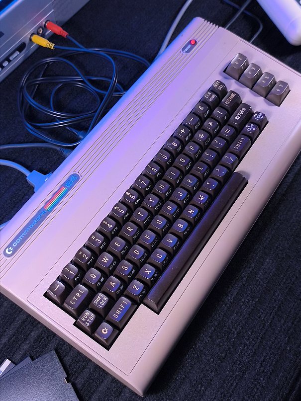 Un Commodore 64 collegato ai cavi, ripreso di tre quarti.