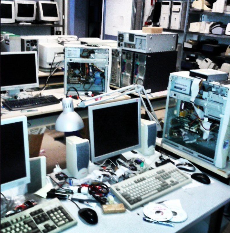 Banco di lavoro con case aperti, tastiere, monitor e componenti smontati.